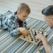 Smart child is playing chess board game with father middle-aged man in casual clothing spending free time at home. Leisure, family and childhood concept.
