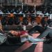 A man and woman resting together on the gym floor, surrounded by dumbbells.